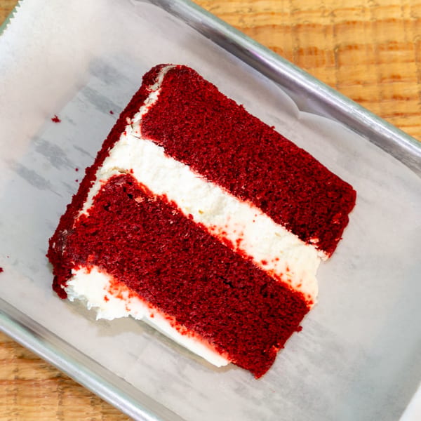 Two slices of red velvet cake with white cream cheese frosting on a metal tray.