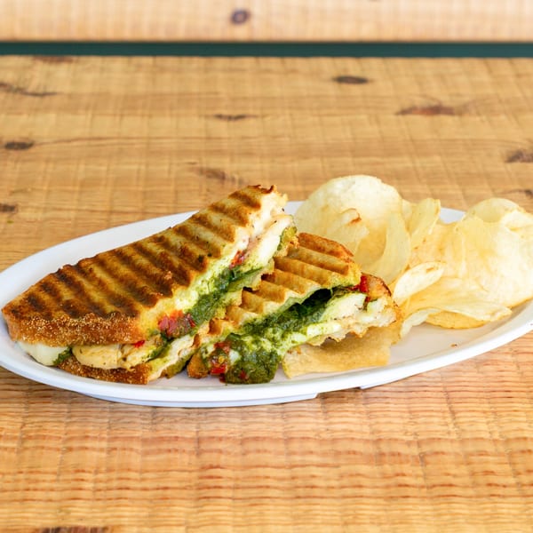 Grilled chicken pesto panini with melted cheese and potato chips on a white plate.