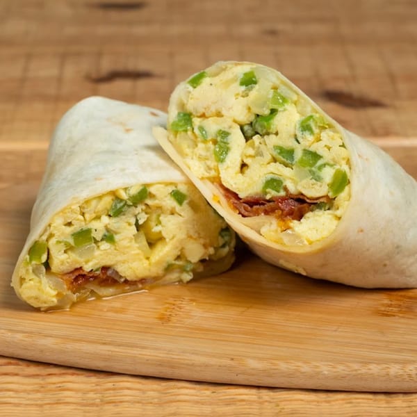 Two halves of a breakfast burrito filled with scrambled eggs, green peppers, and bacon on a wooden board.