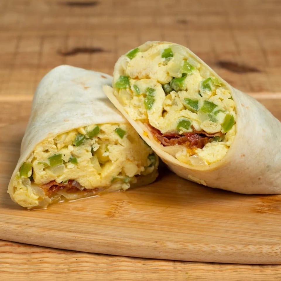 Two halves of a breakfast burrito filled with scrambled eggs, green peppers, and bacon on a wooden board.