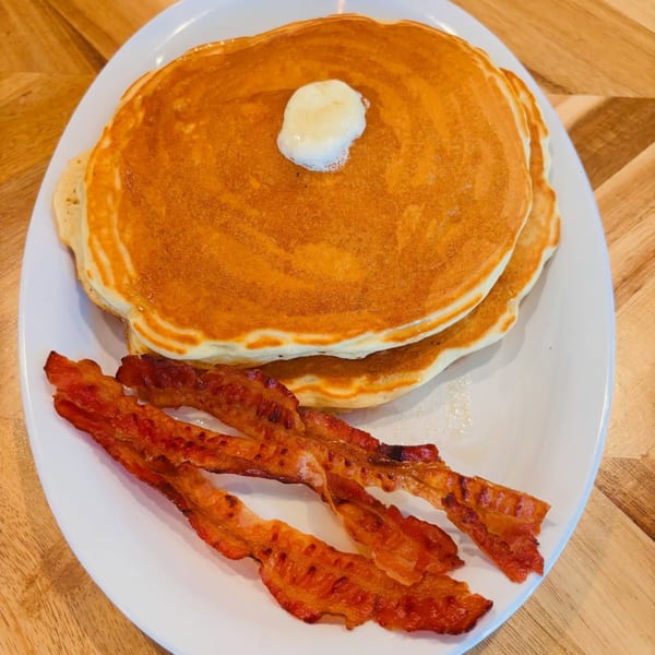 Fluffy pancakes with a dollop of butter and three strips of crispy bacon on a white plate.