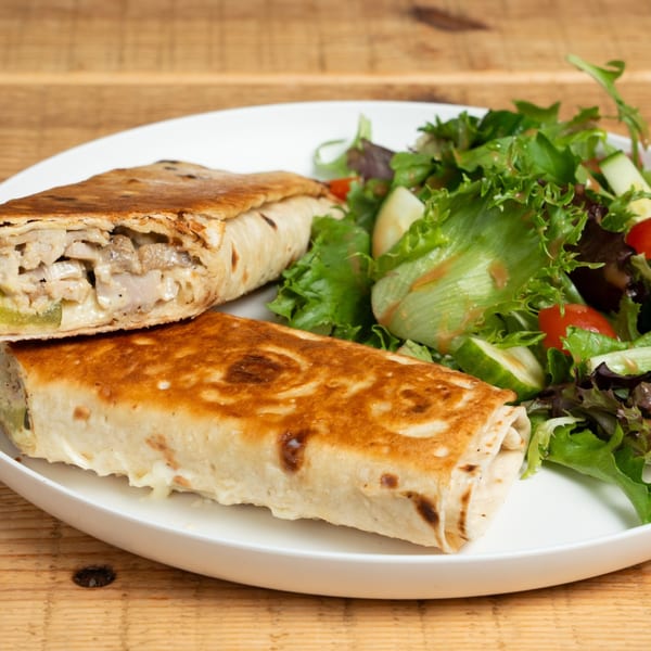 Two grilled wraps, one cut open, revealing chicken and cheese, served with a side salad.