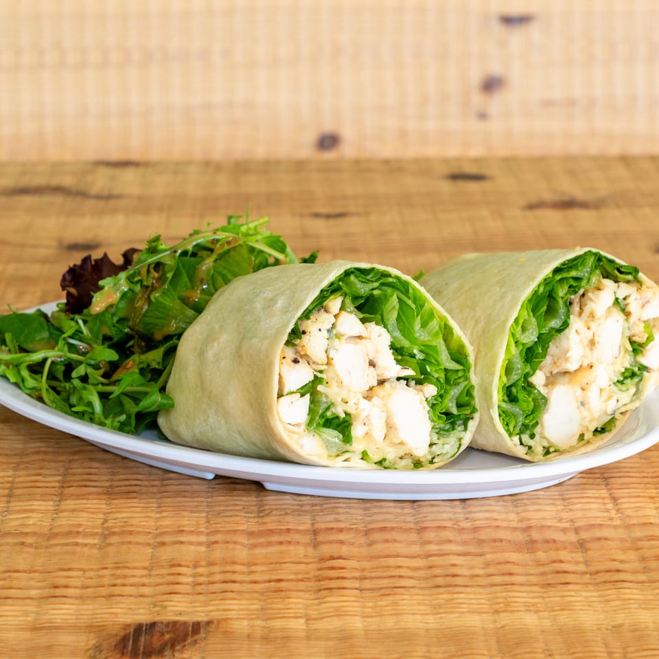 Two chicken Caesar wraps with fresh green lettuce and dressing, served with a side salad.