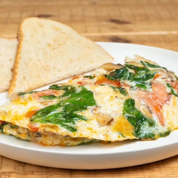 A fluffy omelet filled with spinach, mushrooms, and tomatoes, served with two slices of toast.