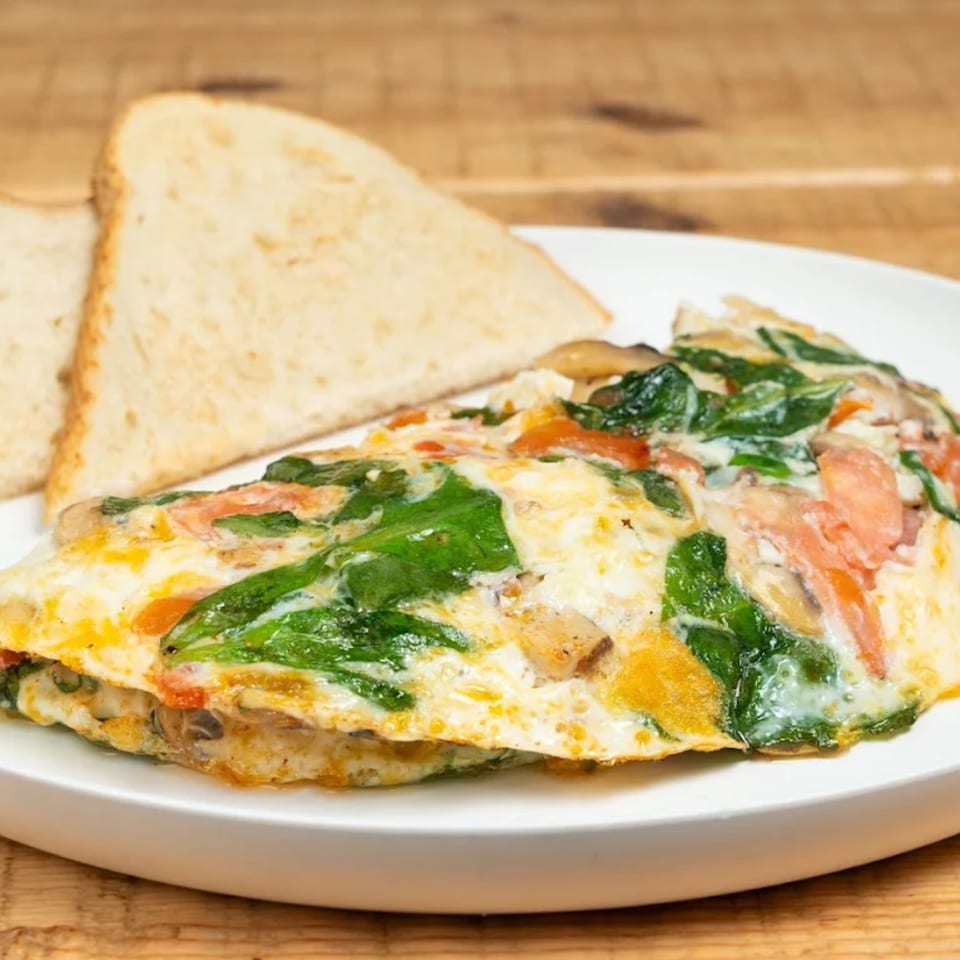 A fluffy omelet filled with spinach, mushrooms, and tomatoes, served with two slices of toast.