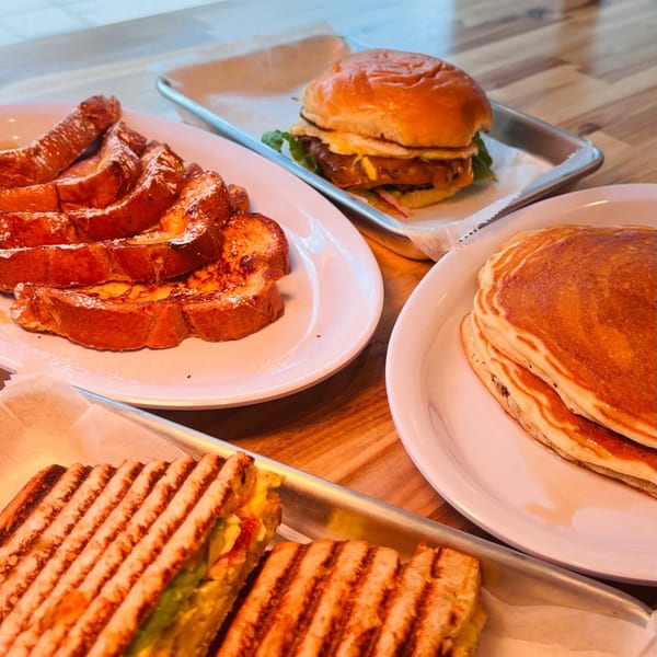 A cafe spread with French toast, pancakes, a burger, and a panini on a wooden table.