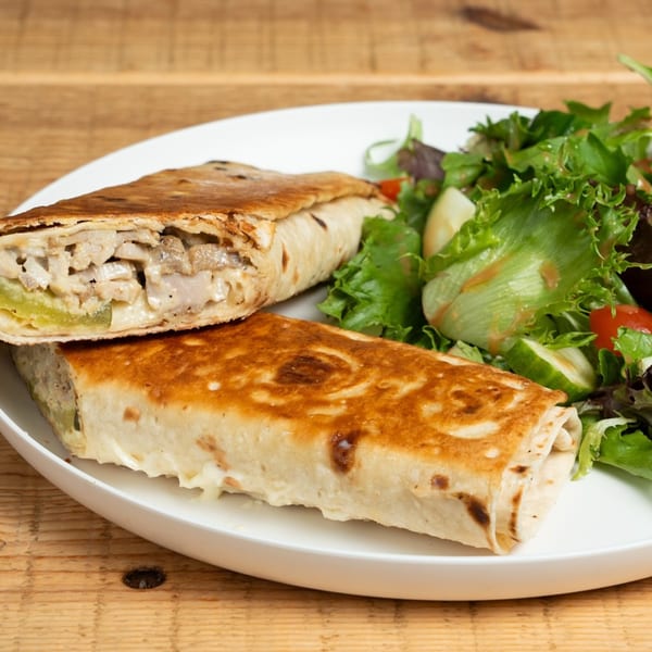 Two grilled wraps filled with chicken and vegetables, served with a side salad on a white plate.