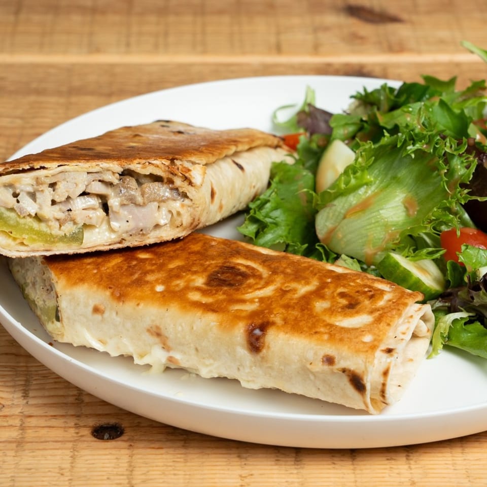 Two grilled wraps filled with chicken and vegetables, served with a side salad on a white plate.
