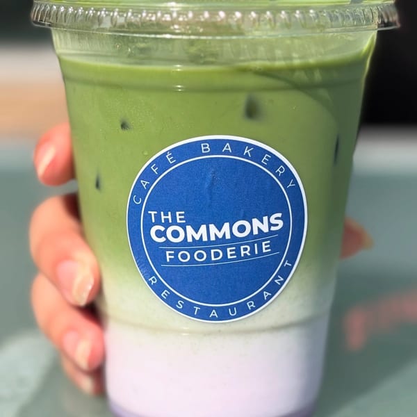 Hand holding a plastic cup of The Commons Fooderie's layered green and purple iced drink.