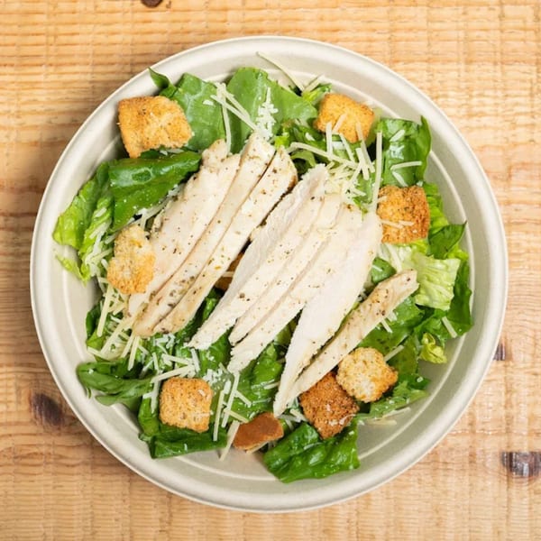 Overhead view of a chicken Caesar salad with romaine, croutons, and parmesan in a bowl.