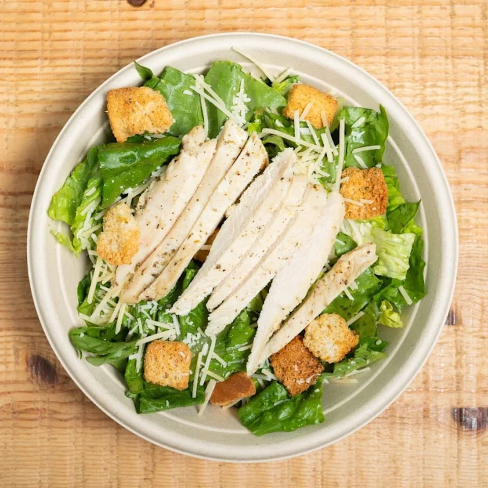 Overhead view of a chicken Caesar salad with romaine, croutons, and parmesan in a bowl.
